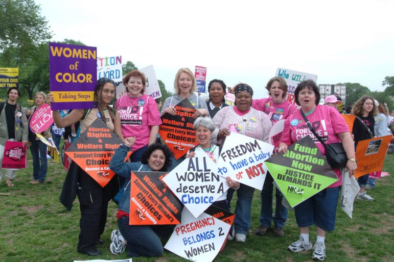 Group of people at a rally hold colorful signs in support of abortion justice and abortion funds.