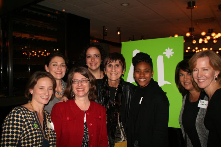 A group of people smile together at an event, standing in front of a green sign with a white design.