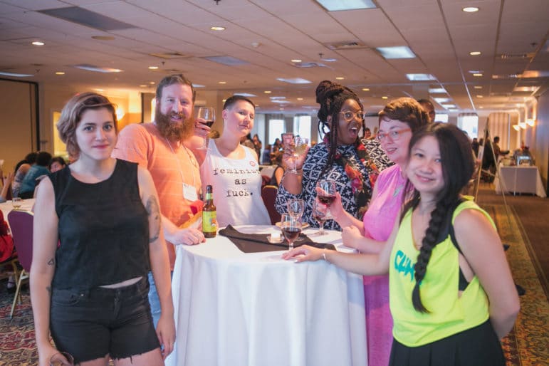 A group of people stand around a tall table, smiling and holding drinks during an abortion funds gathering.