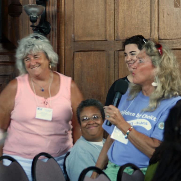 A group of people sit together in a wood-paneled room. One person holds a microphone while others smile and engage in conversation.