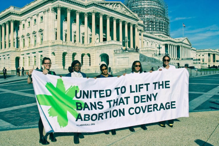 Five people stand in front of the U.S. Capitol holding a banner that reads United to lift the bans that deny abortion coverage, with allaboveall.org printed below.