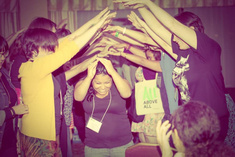 A group forms a tunnel with raised arms as one person walks through, smiling, during an abortion funds gathering.
