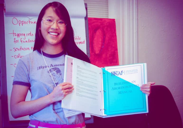 A person smiles while holding open a binder titled Building an Abortion Fund Manual.