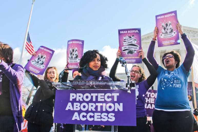 People rally outside the U.S. Supreme Court with signs that say Dear SCOTUS, I had an abortion and a podium banner that reads Protect Abortion Access.